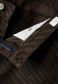 Gros plan sur la ceinture de pantalons en tissu marron montrant le bouton, le trou de bouton, la fermeture éclair et le détail de la doublure intérieure blanche.