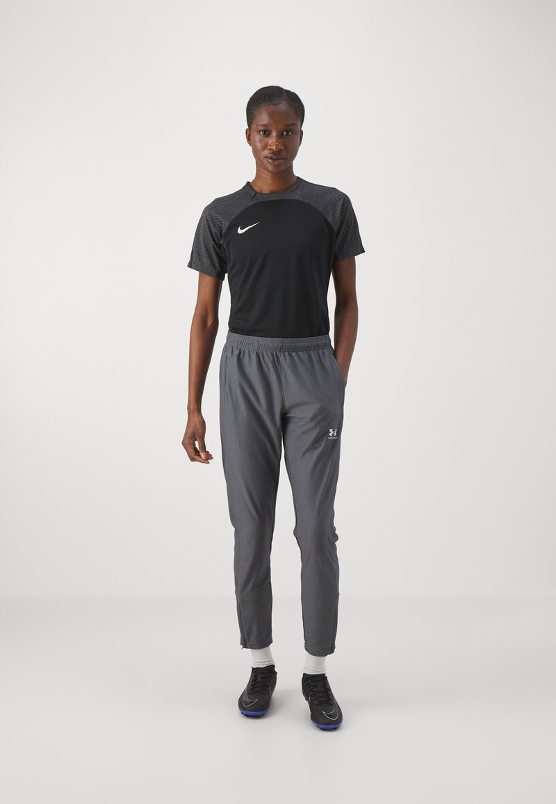 Jersey negra de manga corta con hombros texturizados, pantalones deportivos grises y zapatillas negras con detalles azules, sobre un fondo blanco.