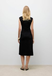 Robe noire ajustée avec des manches courtes, de longueur genou, texture lisse. Portez-la avec des sandales à talons à motifs. Style minimaliste.