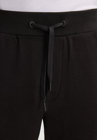 Czarne dresy z teksturowanej tkaniny, elastycznym paskiem w talii oraz sznurkiem do regulacji z plastikowymi końcówkami.