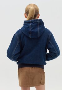 Chaqueta de mezclilla recortada con capucha, color azul oscuro, mangas anchas y dobladillo acanalado. Presenta costuras visibles y una textura suave.