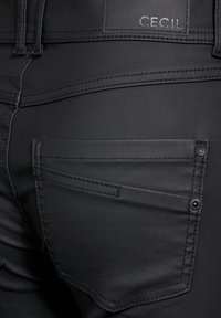 Svarta denimjeans med en mjuk textur, smal design och märkbara syddetaljer. Inkluderar en bakficka med knappprydnader.