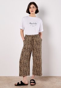T-shirt blanc avec le texte "Peace & Love CLUB", associé à un pantalon large en imprimé léopard beige et des sandales à enfiler noires. Tenue décontractée.