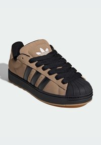 Tenisky s hnedým zvrškom z semišu, čiernou gumovou špičkou, tromi čiernymi pruhmi a čiernymi šnúrkami, s textúrovanou podrážkou.