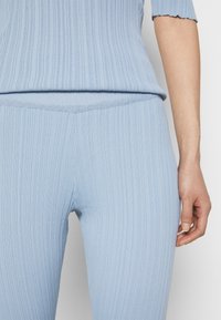 Top en tricot côtelé bleu clair et pantalon taille haute assorti. Gros plan sur la texture et le design ajusté. Détail de l'ourlet en forme de coquille sur les manches.