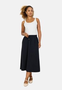 Schwarzer, fließender, knöchellanger Rock mit elastischem Bund und Kordelzug. Kombiniert mit einem weißen Tanktop und hellen Ballerinas.