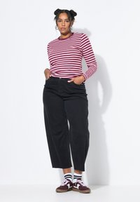 Camisa de rayas burdeos y crema de manga larga combinada con pantalones de mezclilla negros de tiro alto y zapatillas burdeos con detalles en blanco.