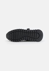 Sort sneakersåle med tekstureret gummi, der har dybe riller og en afrundet hæl. Flad design velegnet til afslappet brug.