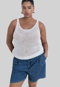 Débardeur tricoté blanc à larges bretelles, associé à un short en denim bleu. Le haut présente un design en tissage ouvert.