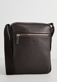 Hnědá kožená crossbody taška s hladkým povrchem, přední kapsou na zip, nastavitelným popruhem a raženým logem na přední straně.