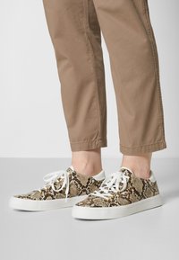 Brown and beige snake print sneakers with white rubber soles and laces, featuring metal eyelets and a textured finish.