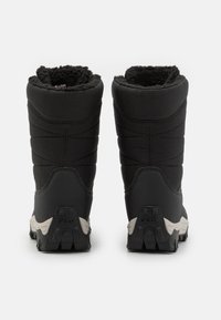 Las botas negras impermeables cuentan con un forro de piel sintética y una parte superior de tela texturizada. La suela es resistente, con patrones de tracción distintivos y detalles de marca.