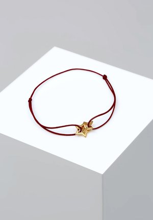Red cord bracelet featuring a gold star charm with a polished finish and layered design. Adjustable knot for size customization.