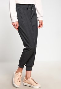 Grå sweatpants med dragsko i midjan, smalnande muddar och sidofickor, kombinerade med ljusa sneakers. Mjuk tygkänsla.