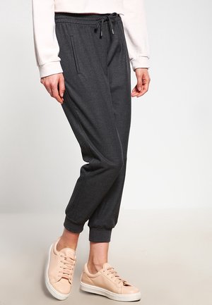 Grijze sweatpants met een trekkoord in de taille, taps toelopende boorden en zijzakken, gecombineerd met lichtgekleurde sneakers. Zachte stoftextuur.