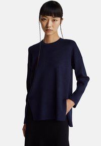 Granatowy sweter dzianinowy z długimi rękawami, okrągłym dekoltem i bocznymi rozcięciami. Charakteryzuje się luźnym krojem oraz widoczną kieszenią z przodu.