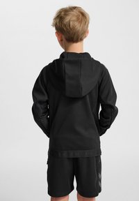 Svart huvtröja med en slät textur, med en bred fåll och logodetaljering. Buren med matchande svarta shorts.