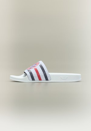 Λευκή σαγιονάρα Adidas με κόκκινες και μαύρες ρίγες και στρογγυλό κόκκινο-μπλε λογότυπο της Bayern Μονάχου στο λουράκι.