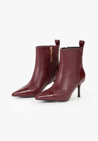 Stivali alla caviglia in pelle bordeaux con punta affusolata, design elegante, zip laterale e tacco sottile. Presentano cuciture a contrasto e una texture liscia.
