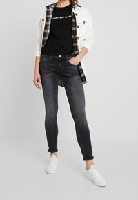 Černé přiléhavé džíny s polo-vysokým pasem a mírným vyšisováním, doplněné černým tričkem s potiskem a bílou džínovou bundou. Bílé tenisky.