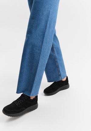 Czarne zamszowe sneakersy o teksturowym wykończeniu, w połączeniu z szerokimi, jasnoniebieskimi dżinsami z surowym wykończeniem i luźnym krojem.