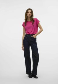 Roze top met korte mouwen, gecombineerd met donkerdenim wijde broek. De stof lijkt glad; de jeans hebben zijzakken en minimale stiksels.
