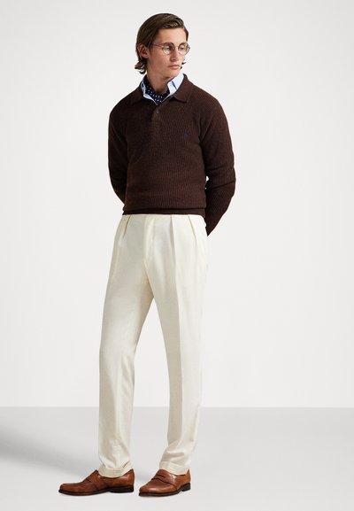 Brun strikkegenser over en lyseblå skjorte, kremfargede bukser og brune skinnsko. Merkbare detaljer inkluderer en strukturert overflate og en krage.