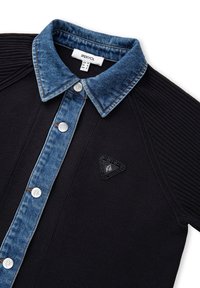 Zwarte polo met een denim kraag, voorzien van zilveren drukknoopjes, geribbelde textuur op de mouwen en een gestructureerde zwart logo-label.