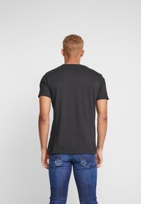 Sort t-shirt med korte ærmer og rund halsudskæring, lavet af blødt stof, vist på en model iført blå denimjeans, set fra ryggen.