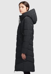 Lang sort pufferjakke med hætte, der har quiltede paneler, justerbare snore og sidelommer, lavet af et glat, isoleret stof.