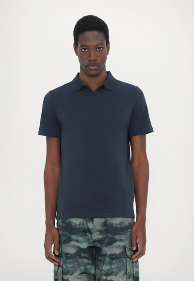 Camiseta polo azul marino de algodón, con un diseño de cuello y mangas cortas, combinada con pantalones de camuflaje.