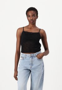 Mustriga must tank top õhukeste rihmadega ja kaelaribadega lipsu detailiga, kombineeritud kõrge vöökohaga helesiniste teksadega.