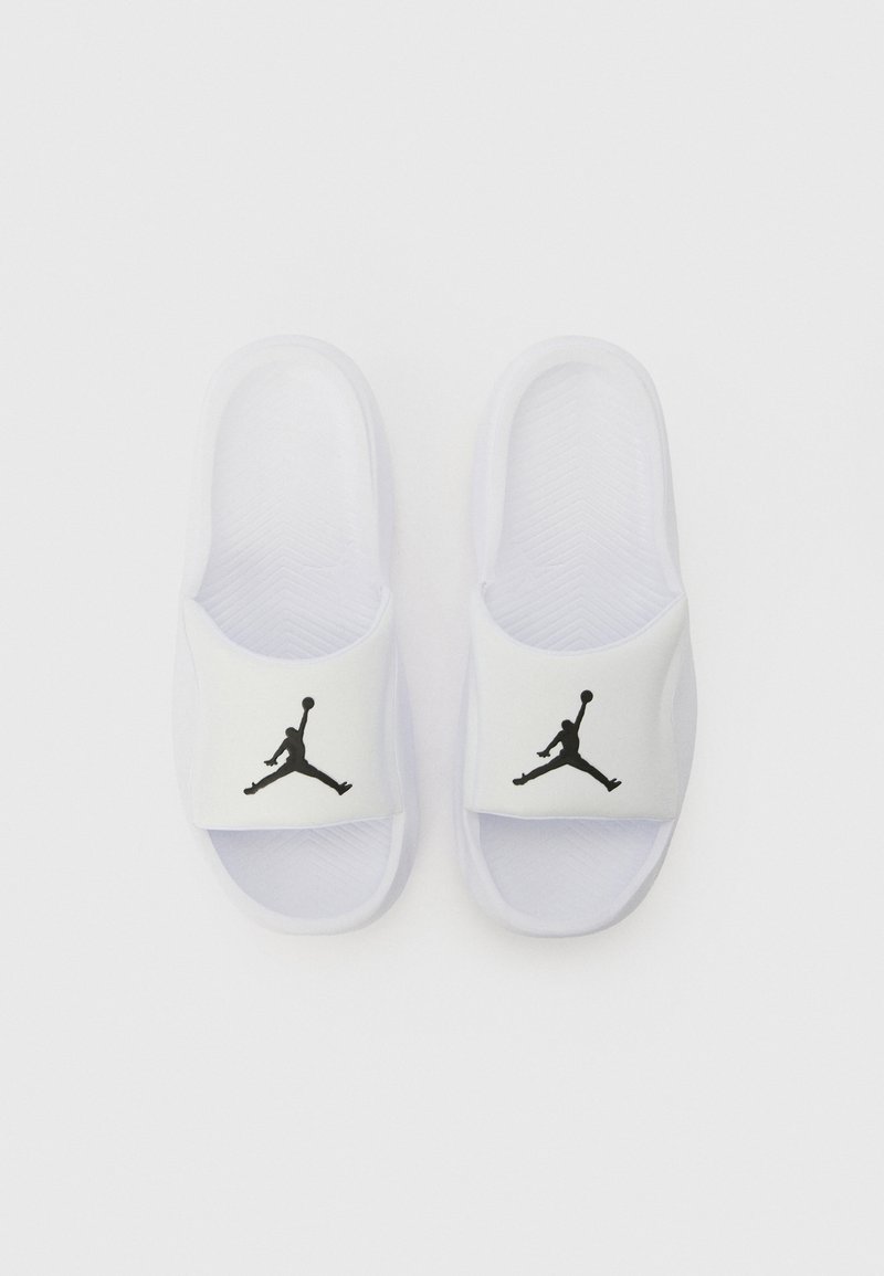 Chanclas blancas con suela texturizada, que presentan un logo Jumpman negro en la correa blanca. Material suave con diseño de punta abierta.