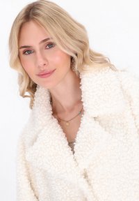 Witte textuur fleece jas met een brede kraag, zachte oppervlakte en een losse pasvorm. Voorzien van een gelaagde gouden ketting met kleine decoratieve elementen.