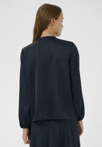 Marineblauwe satijnen blouse met lange mouwen en geplooide manchetten, voorzien van een eenvoudige ronde halslijn en een losse pasvorm, gladde textuur.