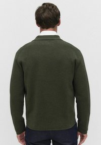 Mörkgrön tröja med krage, strukturerat stickat material, långa ärmar och rundad nederkant, sedd bakifrån.