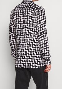 Långärmad skjorta i svart och vitt hundtandsmönster. Har en klassisk krage och en avslappnad passform med uppkavlade ärmslut.