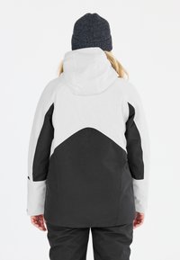 Schwarze und weiße wasserdichte Jacke mit Kapuze, die ein geometrisches Design, strukturierten Stoff und verstellbare Handgelenkabschlüsse aufweist.