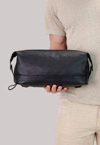 Borsa in pelle nera con finitura testurizzata, forma rettangolare e due manici laterali. Cuciture visibili e un piccolo logo sul lato.