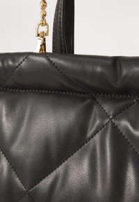 Black leather handbag featuring a quilted design, smooth texture, and gold hardware. The chain strap adds a metallic accent.