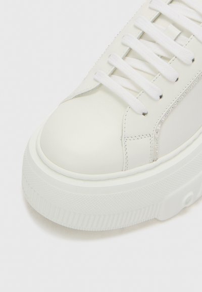 White leather sneaker featuring a rounded toe, flat laces, and textured rubber outsole with decorative rhinestone detailing along the side.