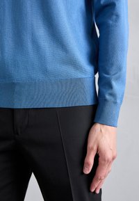 Gai zils džemperis, kas izgatavots no mīksta adījuma materiāla, ar ribinātu apakšmalu un piedurkni. Melni šūti bikses redzamas attēla apakšā.