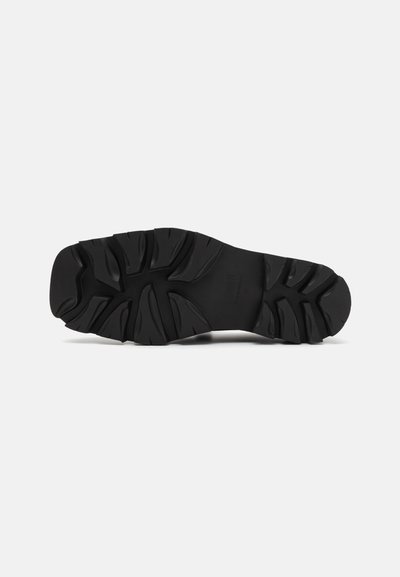 Black rubber shoe sole with deep grooves and patterns for traction, featuring a rounded toe and curved heel design.