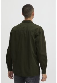 Camicetta button-up verde scuro con colletto, maniche lunghe e vestibilità rilassata. Il tessuto sembra morbido con una leggera lucentezza.