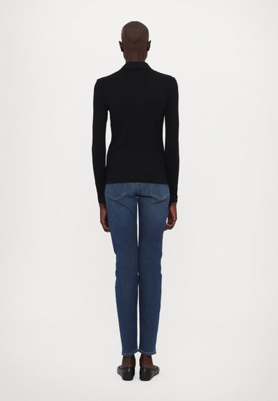 Svart ribbet langermet topp kombinert med blå denim jeans som sitter tett, med middels høy midje og rett ben. Svartsko.