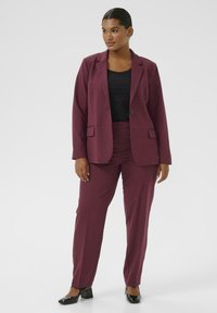 Bordeauxfarbener Blazer und passende maßgeschneiderte Hose aus glattem Material, kombiniert mit einem schwarzen Oberteil. Verfügt über strukturierte Reverskragen und seitliche Taschen.