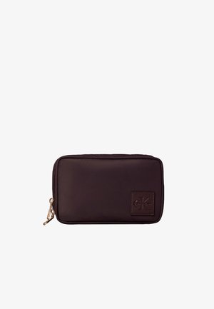 Mała prostokątna ciemnobrązowa saszetka na zamek z złotym suwakiem i tłoczonym logo Calvin Klein na przednim rogu.