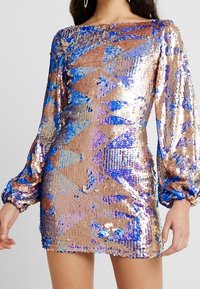 Kortsleeved, åtsittande klänning i paljettmaterial med geometriska mönster i guld, blått och silver. Slät textur; lätt glans.