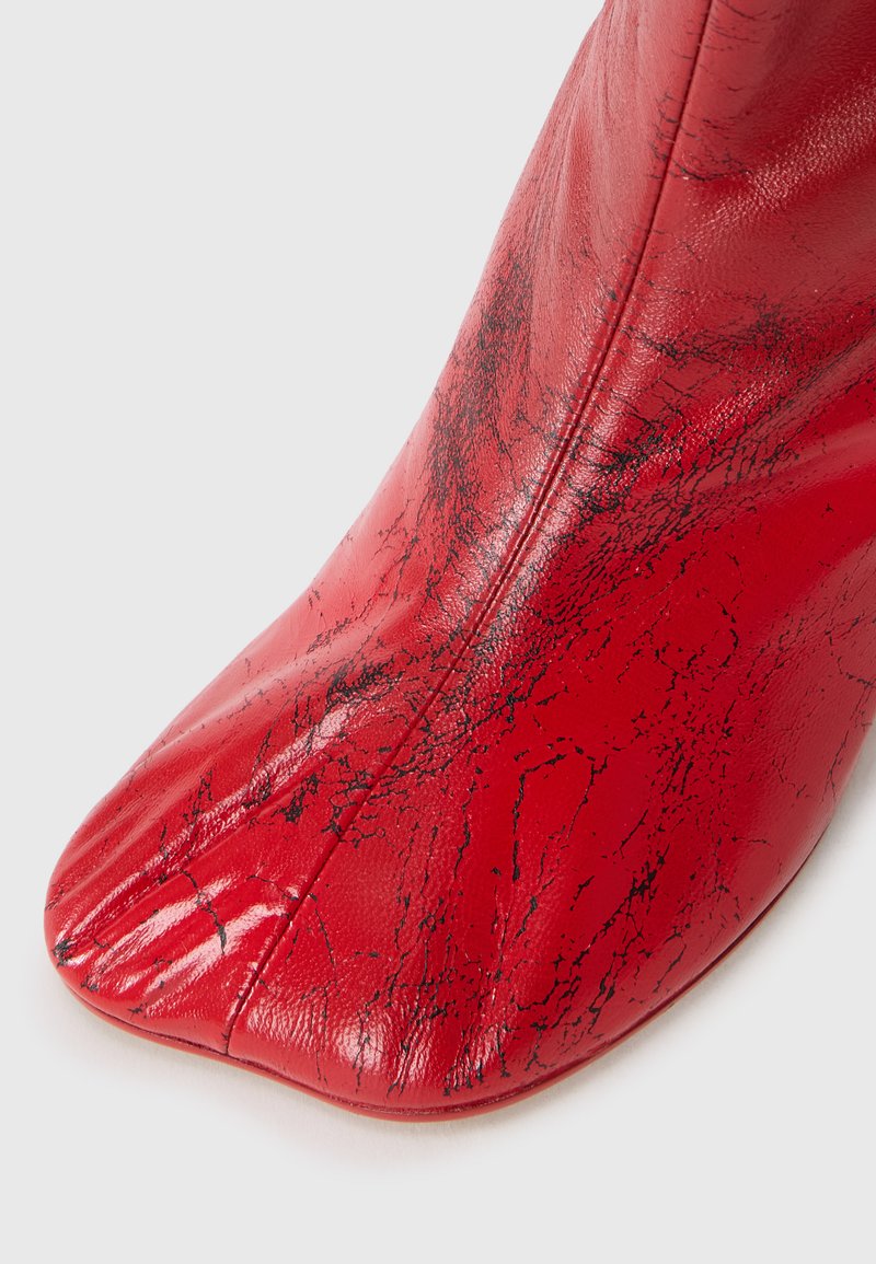 Crimson red leather ankle boot with a pointed toe, featuring a textured crackle pattern and a smooth finish. Zipper along the side.