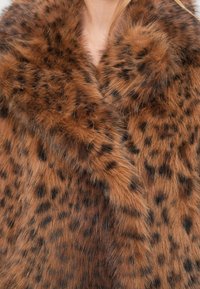 Brauner Kunstpelzmantel mit dunklen Flecken, versehen mit einem breiten Kragen und einem weichen, strukturierten Finish. Das Design imitiert ein Tiermuster.